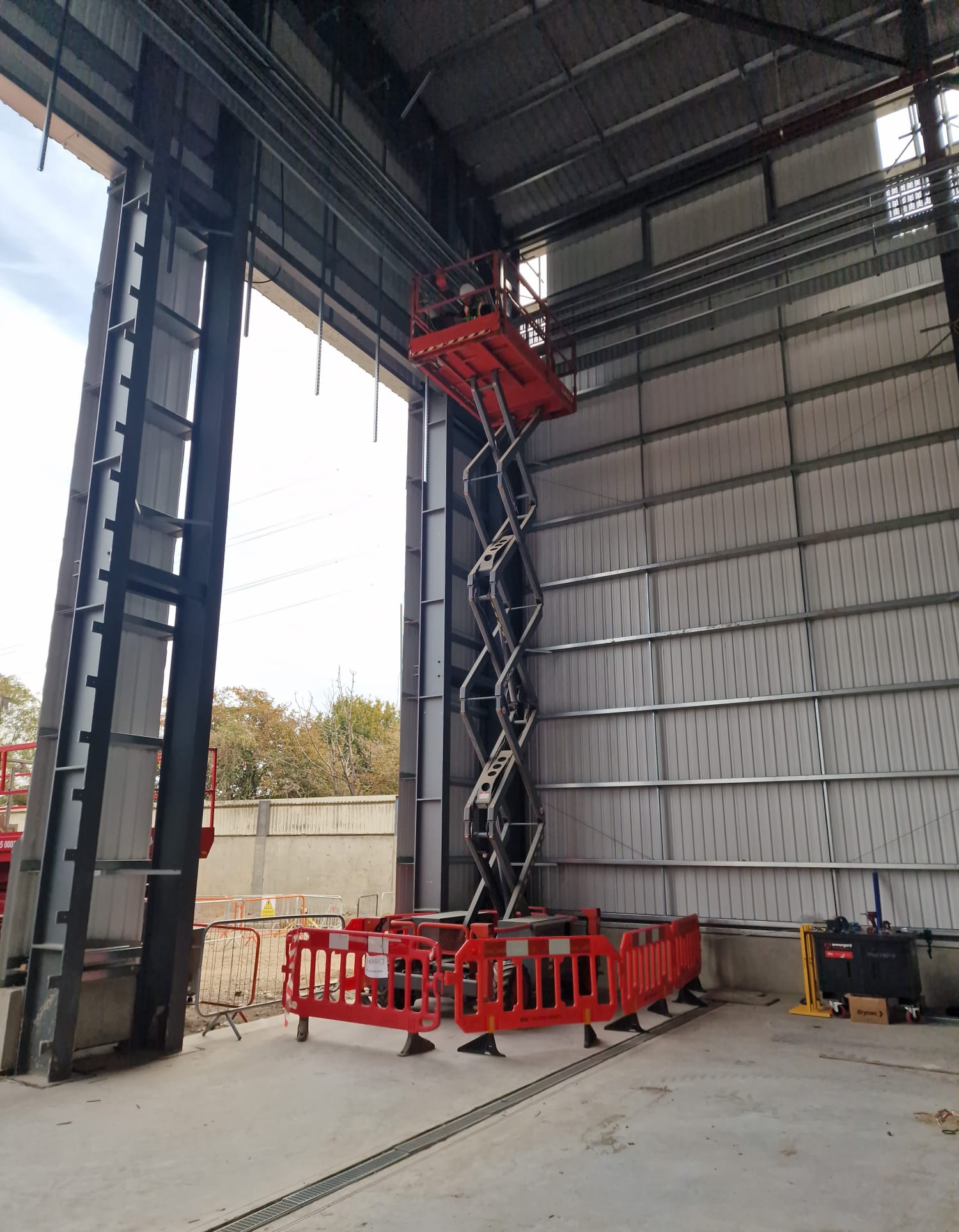 Extended scissor lift inside the main building, with barriers around its base