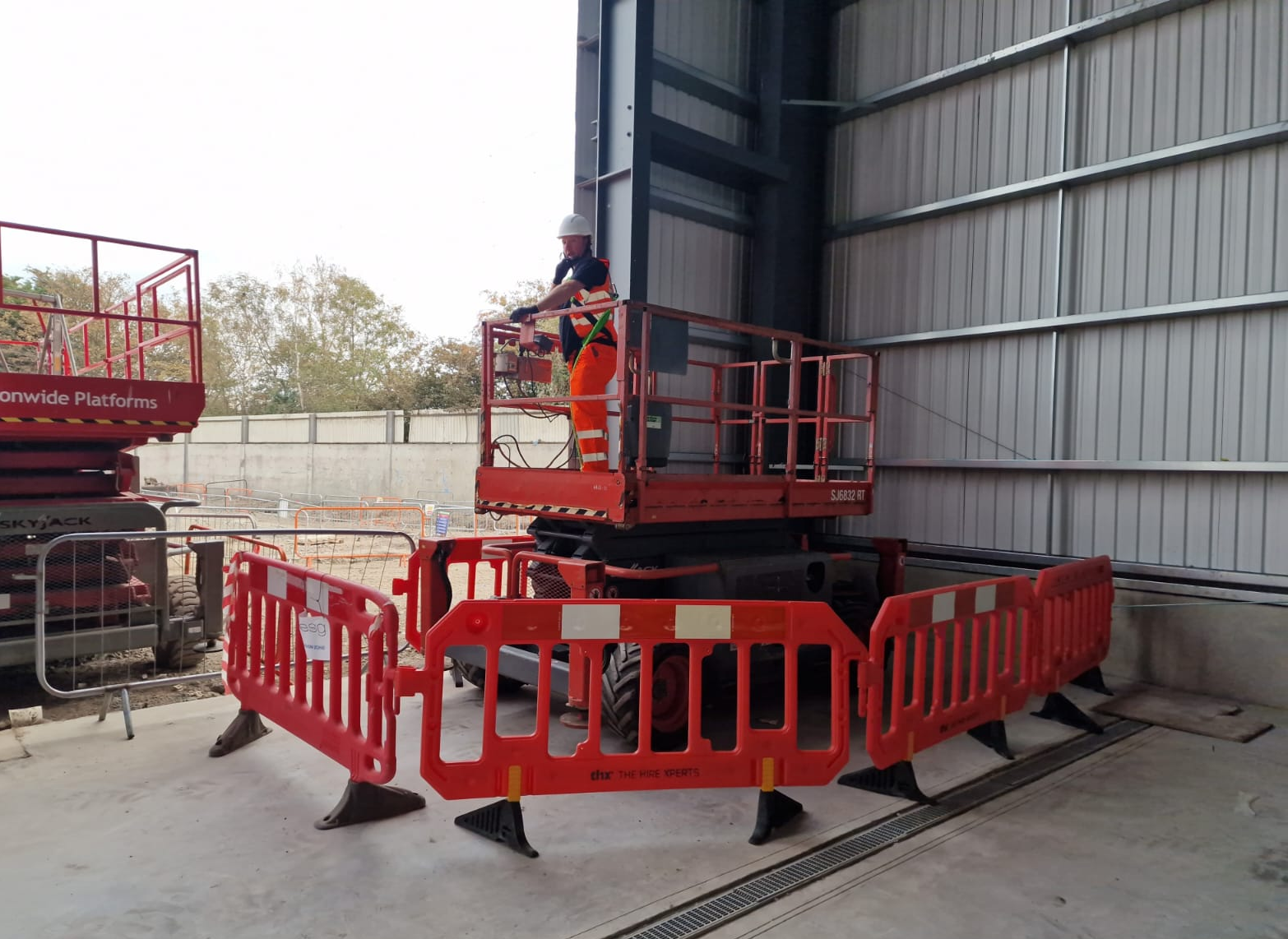 Site operative on a scissor-lift platform within a barriered work area