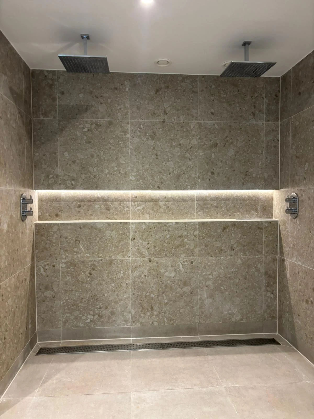 Twin overhead showers with wall controls and a linear floor drain