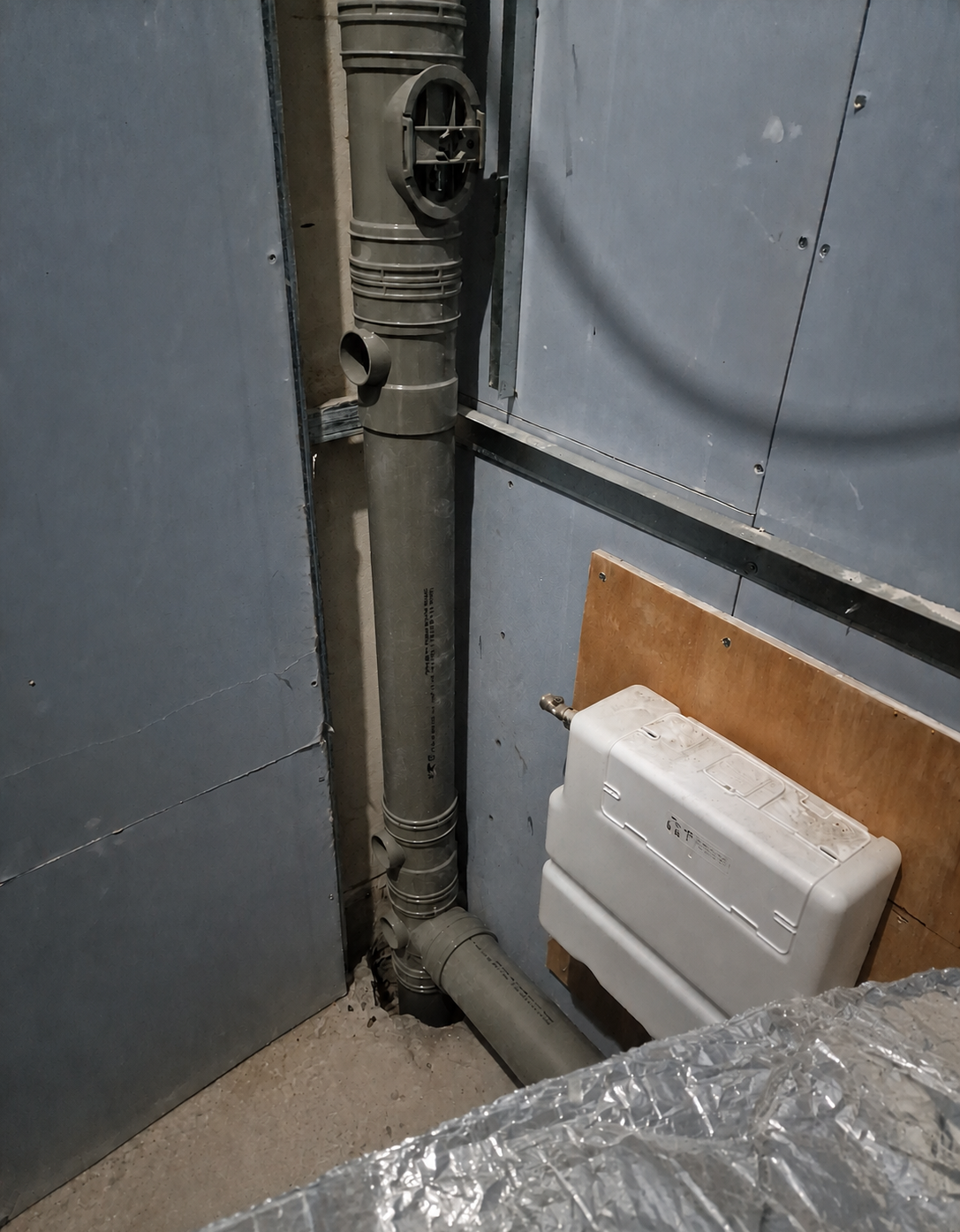 Grey drainage pipework beside a concealed WC cistern during first fix