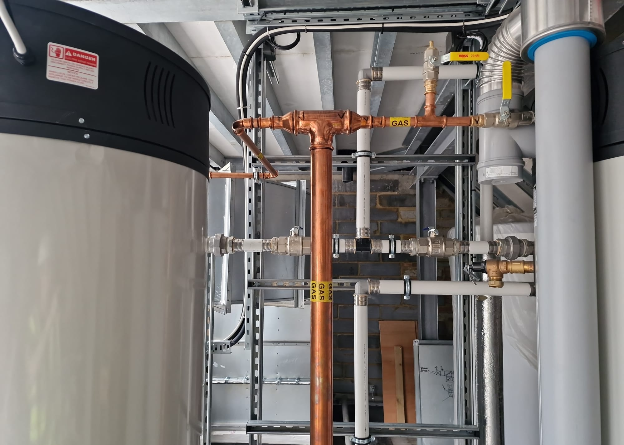 Labelled copper gas pipework and white water pipework between rooftop water heaters