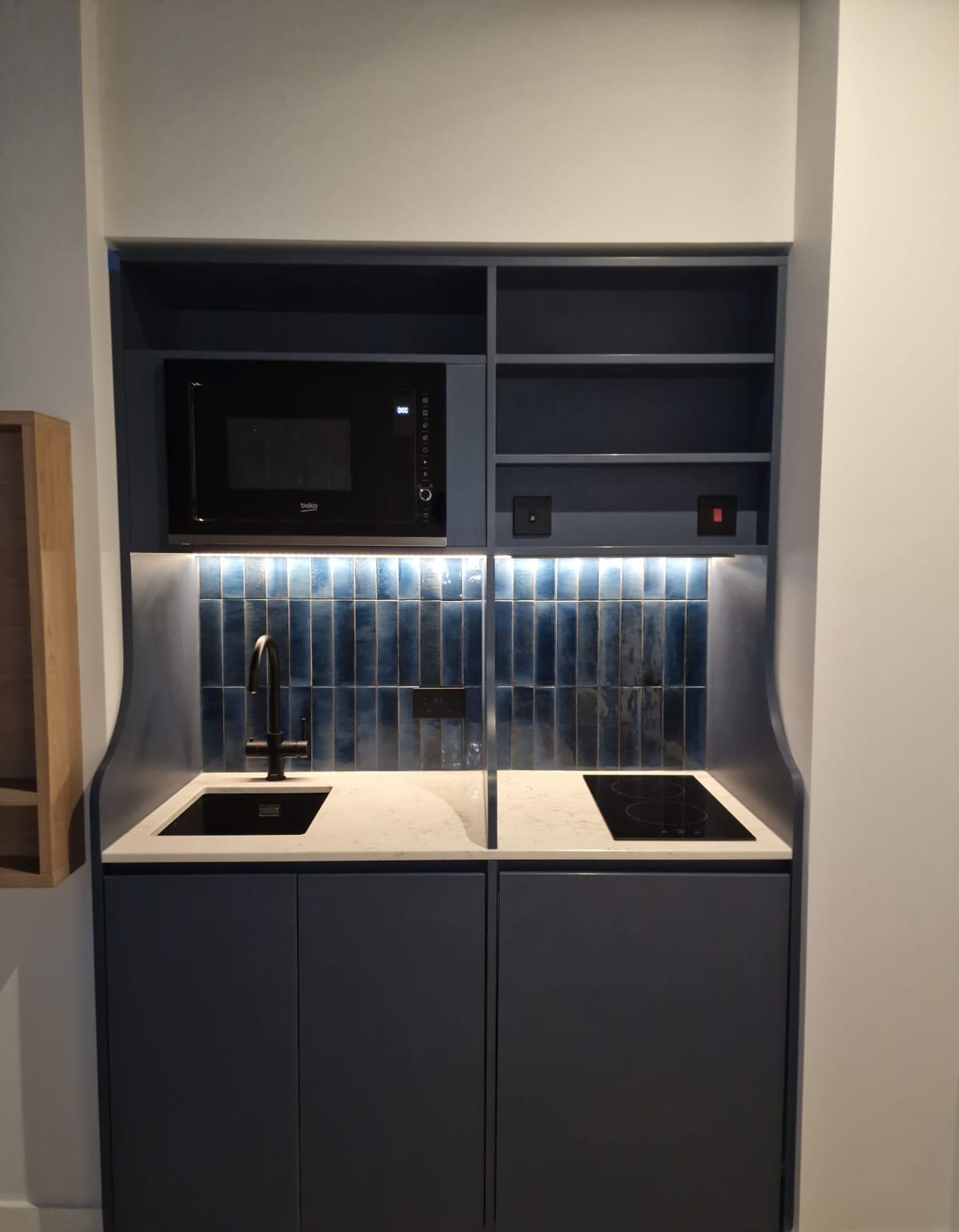 Kitchenette with black sink and tap within blue cabinetry