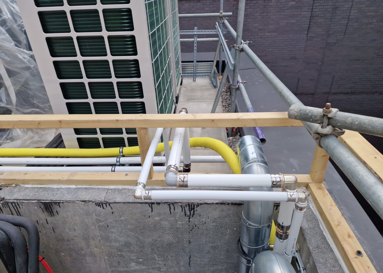 White multilayer pipework and yellow gas pipework at roof level during installation