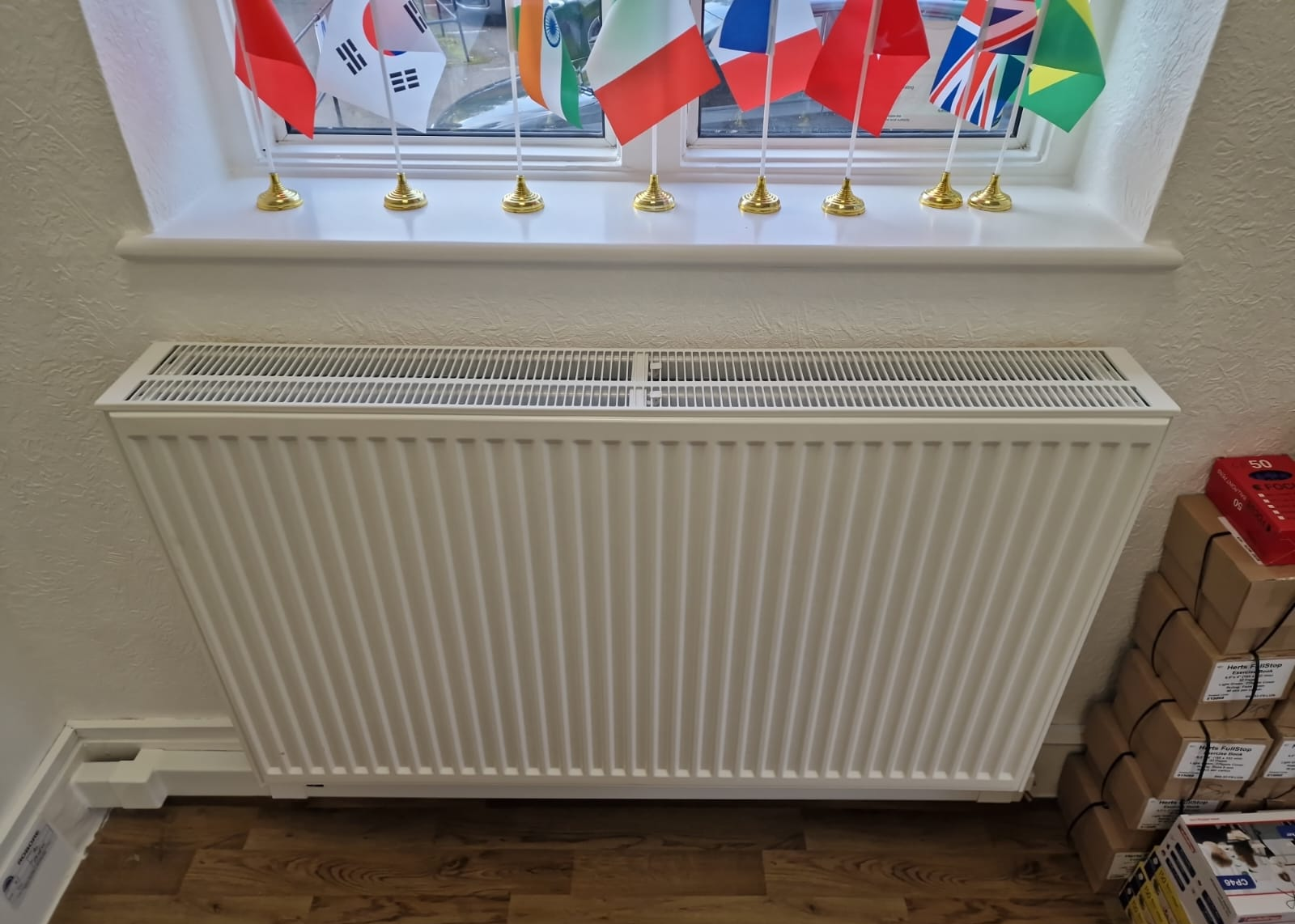 White radiator below a window with enclosed pipework