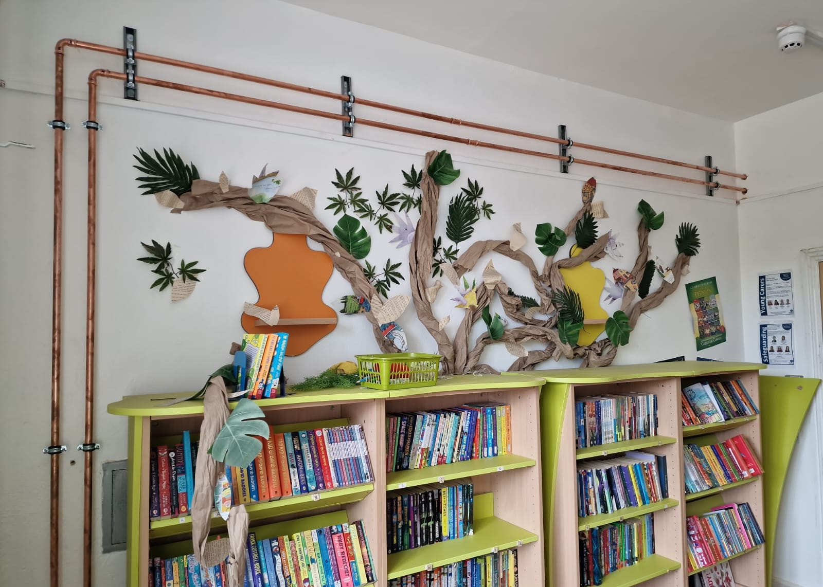 Copper heating pipework routed above library bookshelves
